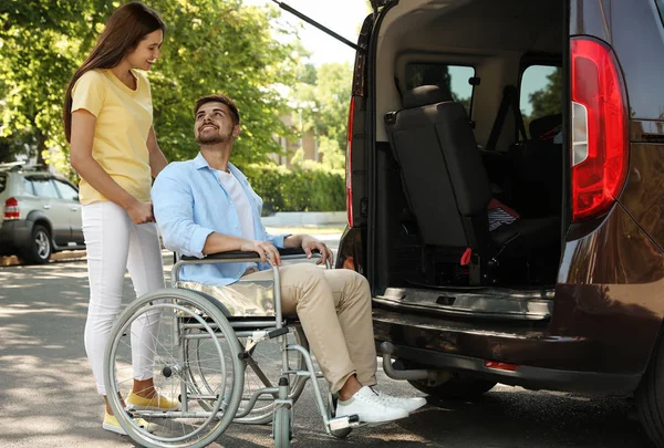 Młoda kobieta pomaga człowiekowi w wózku, aby dostać się do van na zewnątrz — Zdjęcie stockowe