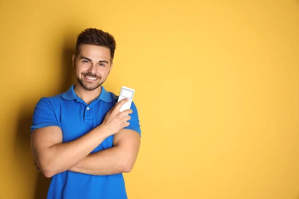 Jovem feliz com ar condicionado controle remoto no fundo amarelo. Espaço para texto — Fotografia de Stock