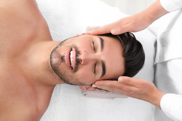 Schöner junger Mann erhält Gesichtsmassage auf Wellness-Tisch, Draufsicht — Stockfoto