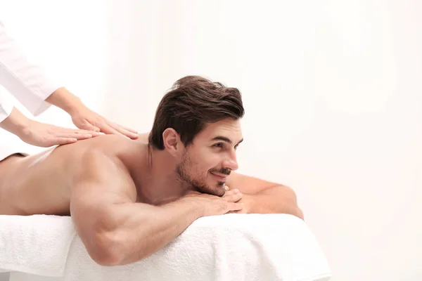 Przystojny młody człowiek odbiera masaż pleców na jasnym tle, miejsce na tekst. Salon Spa — Zdjęcie stockowe
