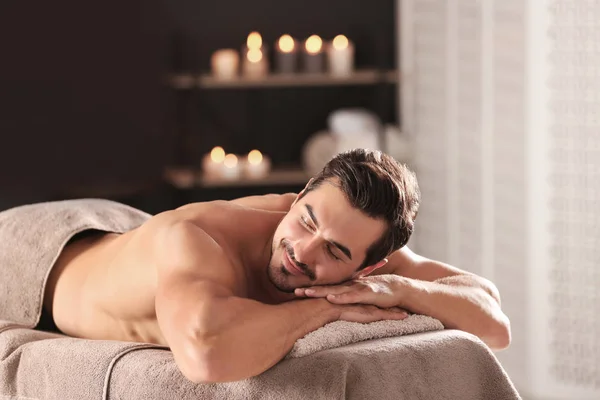 Przystojny młody człowiek relaks na stole do masażu w salonie Spa, miejsce na tekst — Zdjęcie stockowe