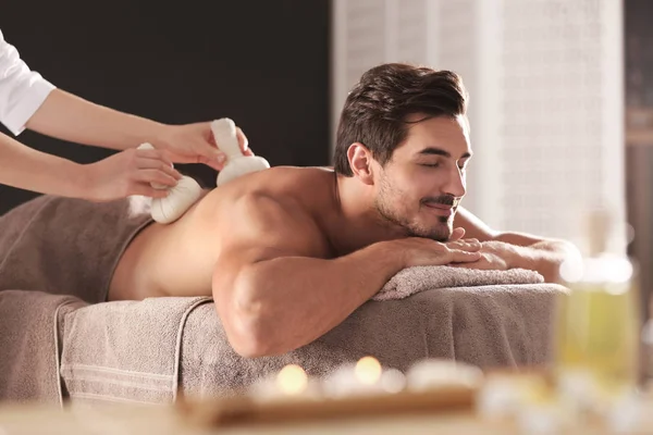 Schöner junger Mann erhält Kräuterbeutel-Massage im Wellness-Salon — Stockfoto