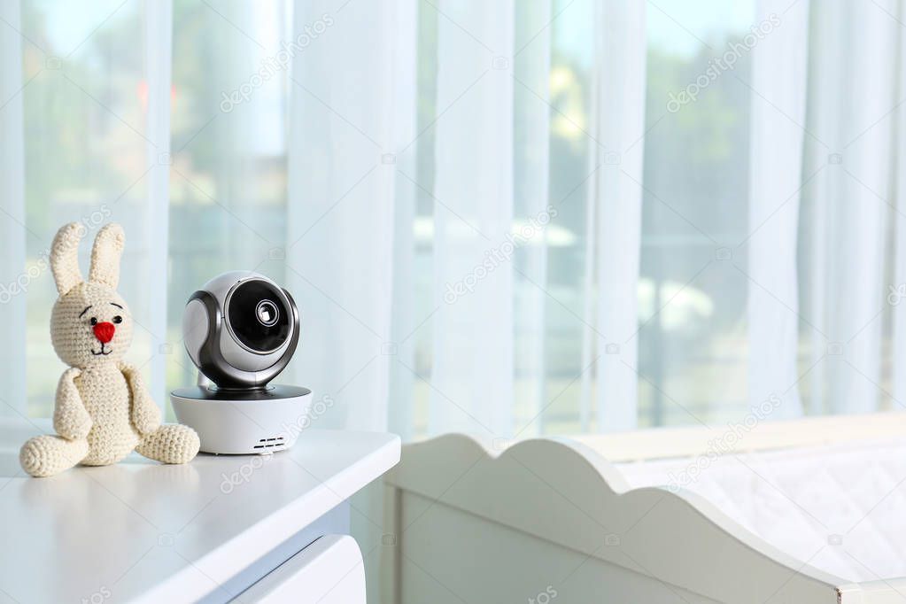 Baby camera with toy on chest of drawers in room, space for text. Video nanny