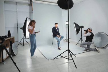 Asistan modern stüdyoda genç adamın fotoğrafını çeken profesyonel fotoğrafçı