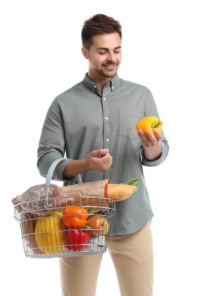 Junger Mann mit Paprika und Einkaufskorb voller Produkte auf weißem Grund — Stockfoto