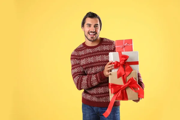 穿着圣诞毛衣和帽子的快乐男人在黄色背景上拿着礼品盒 — 图库照片