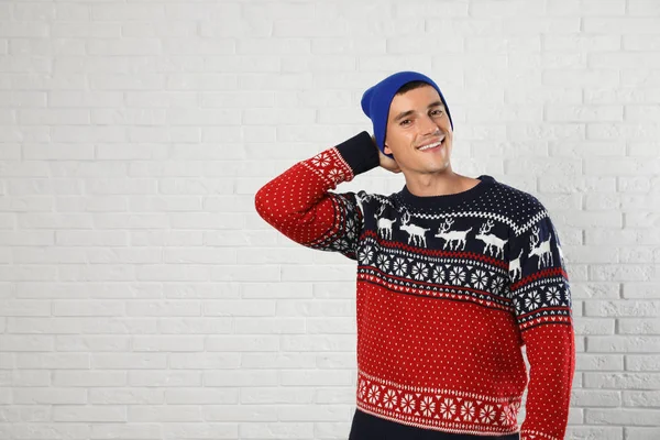 Portrait of young man in Christmas sweater and hat near white brick wall. Space for text — Stock Photo, Image