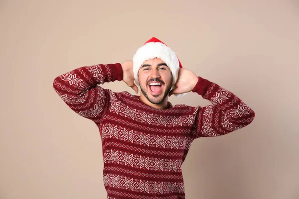 Portrait of young man in Christmas sweater and Santa hat on beige background — Stock Photo, Image