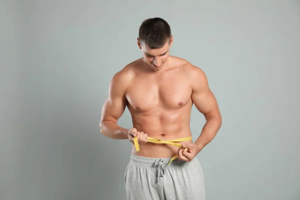 Jovem com corpo magro usando fita métrica em fundo cinza — Fotografia de Stock