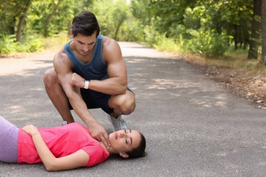 Genç adam parkta baygın bir kadının nabzını kontrol ediyor. Metin için alan