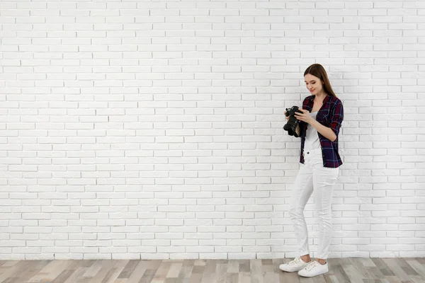 Fotógrafo profissional com câmera moderna perto da parede de tijolo branco. Espaço para texto — Fotografia de Stock