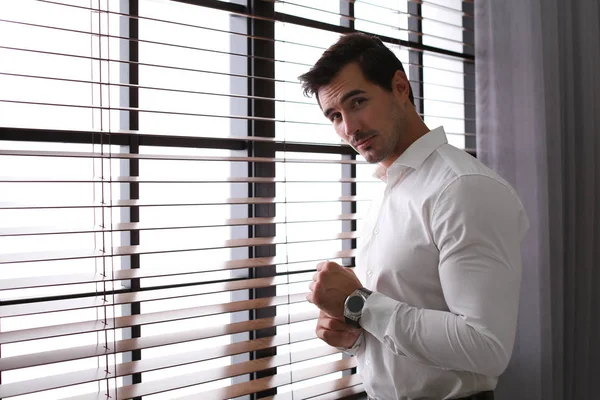 Handsome young man in white shirt standing near window indoors