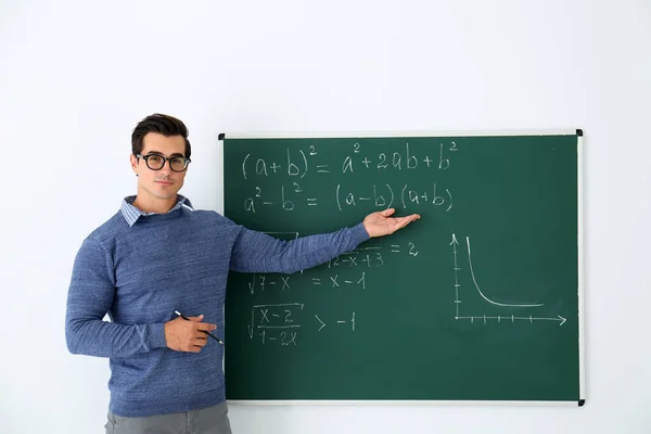 Giovane insegnante che spiega le formule matematiche scritte sulla lavagna in classe — Foto Stock