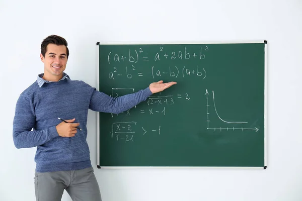 Guru muda menjelaskan rumus matematika yang tertulis di papan tulis di kelas — Stok Foto