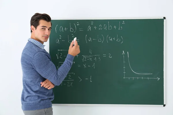 年轻的老师在黑板旁，教室里有数学公式 — 图库照片