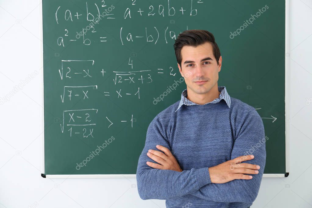 Young teacher near chalkboard with math formulas in classroom