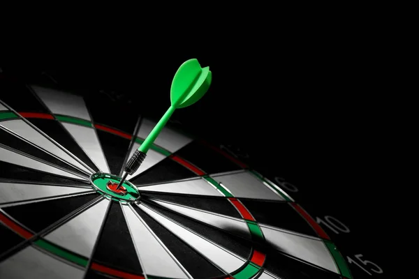 Green arrow hitting target on dart board against black background. Space for text