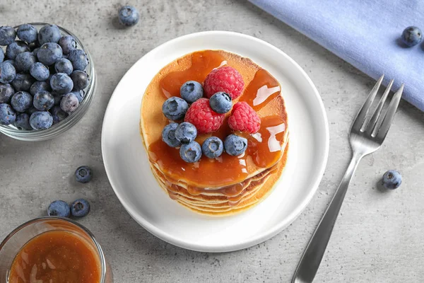 Deliciosos panqueques con bayas frescas y almíbar servidos sobre mesa gris, por encima de la vista — Foto de Stock