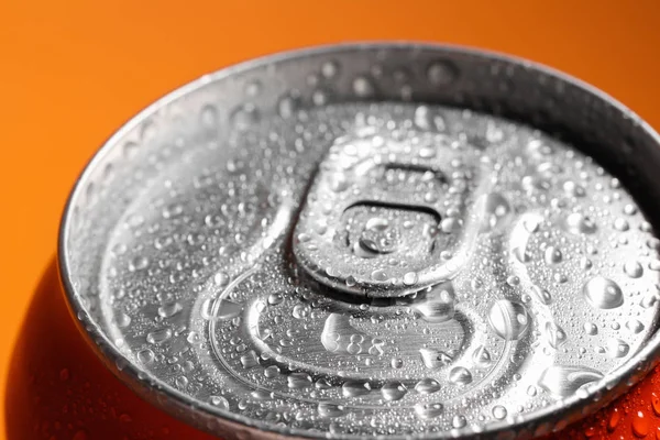 Lata de alumínio de bebida coberta com gotas de água no fundo laranja, close-up — Fotografia de Stock