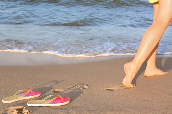 Primer plano de mujer y chanclas en arena cerca del mar, espacio para el texto. Accesorios de playa — Foto de Stock