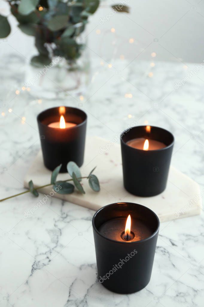 Burning candles and green branch on marble table