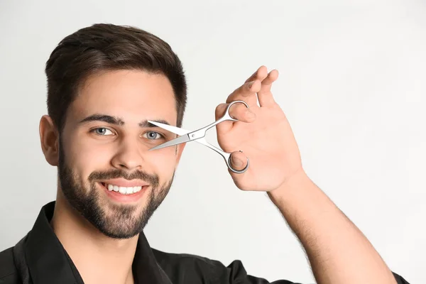 Молодий перукар тримає професійні ножиці на світлому фоні — стокове фото