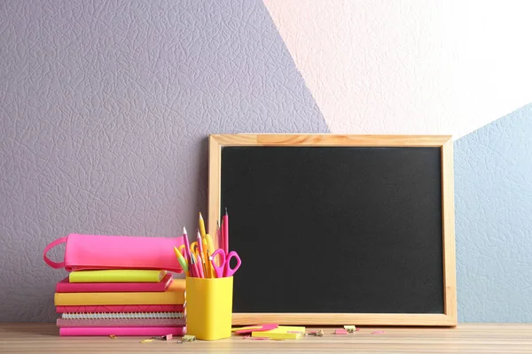 Verschiedene Schulschreibwaren und kleine leere Kreidetafel auf einem Tisch neben der Wand. Raum für Text — Stockfoto