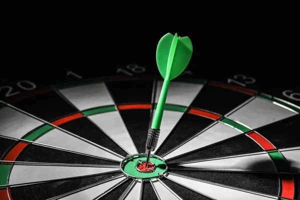 Green arrow hitting target on dart board against black background — Stock Photo, Image