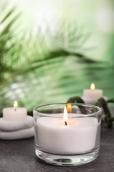 Hořící svíčku ve skleněném držáku na šedý stůl proti rozmazané zelené pozadí, prostor pro text — Stock fotografie