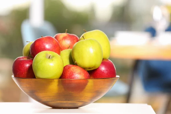 Bowl with different sweet apples on table in room, closeup
