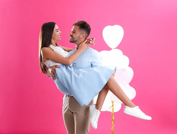 Pareja joven y globos aéreos sobre fondo rosa. Celebración del Día de San Valentín — Foto de Stock