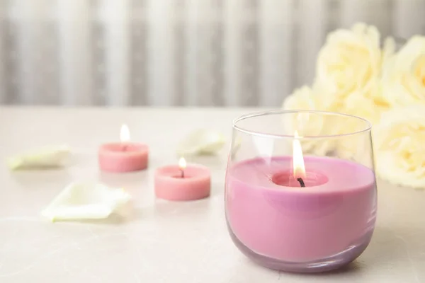 Hořící svíčka ve skleněném držáku a růžích na lehčím stole, prostor pro text — Stock fotografie