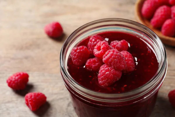 Glazen potje zoete jam met rijpe frambozen op houten tafel, close-up — Stockfoto