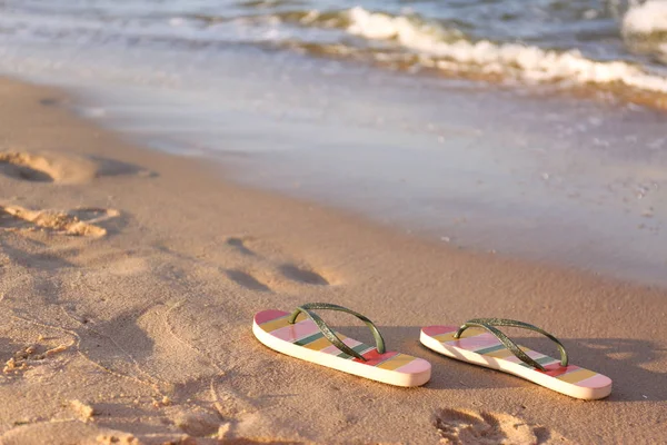 Des tongs élégantes sur le sable près de la mer, espace pour le texte. Accessoires de plage — Photo