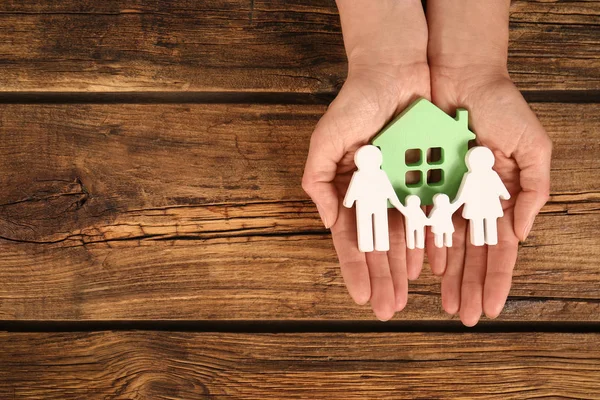 Vrouw het houden van cijfers van familie en groen huis in handen op houten achtergrond, Top uitzicht. Ruimte voor tekst — Stockfoto