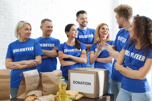Equipo de voluntarios cerca de la mesa con donaciones de alimentos en el interior — Foto de Stock