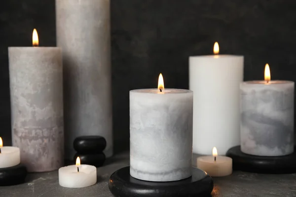 在灰色的桌子上燃烧蜡烛和黑色水疗石 — 图库照片