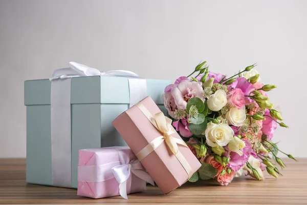 Piękny bukiet kwiatów i pudełka prezentowe na drewnianym stole przed jasnym tłem — Zdjęcie stockowe