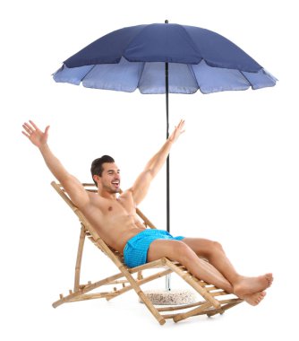 Beyaz arka plana karşı şemsiye altında şezlonsun üzerinde genç adam. Plaj aksesuarları