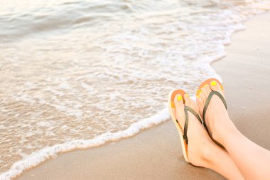 Denize yakın kum üzerinde şık parmak arası terlik ile kadın closeup, metin için alan. Plaj aksesuarları