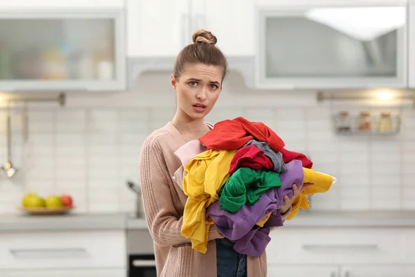 Woman holding pile of dirty laundry in kitchen — Stock Photo, Image