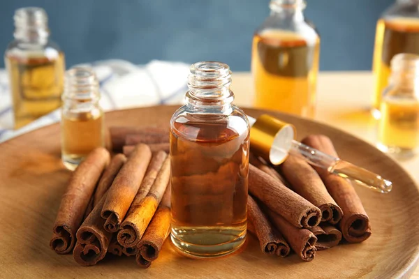 Botellas de aceites esenciales y varillas de canela en placa de madera, primer plano — Foto de Stock