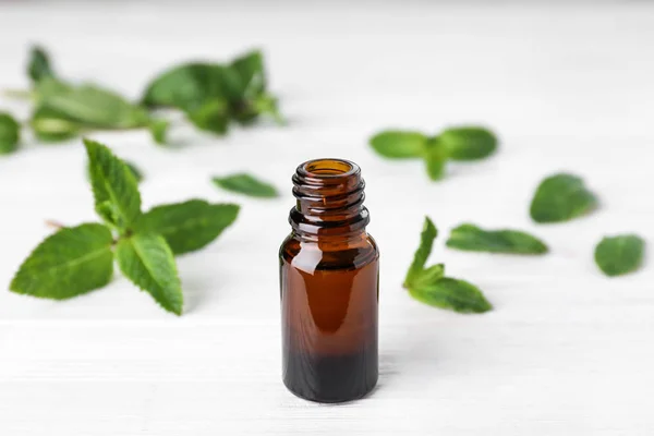 Bottle of mint essential oil on white wooden table — Stock Photo, Image