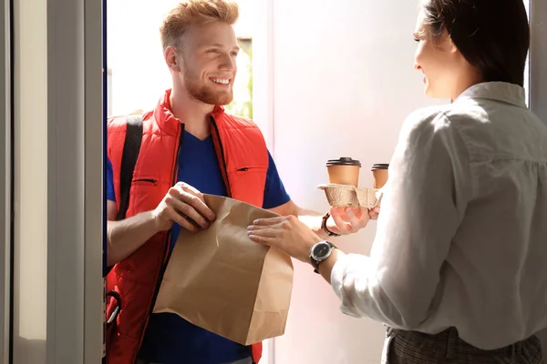 Koerier geeft orde aan jonge vrouw bij open deur. Food delivery service — Stockfoto