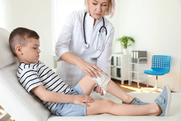 Doctor applying medical bandage to little patient's injured knee in clinic