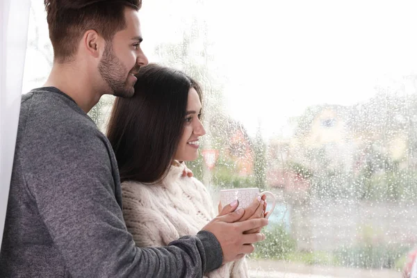 Šťastný mladý pár blízko okna za deštivého dne — Stock fotografie