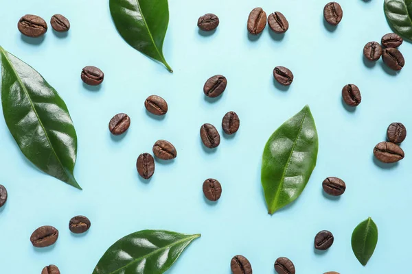Fresh green coffee leaves and beans on light blue background, flat lay