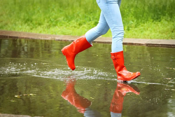 赤いゴムのブーツを持つ女性は、水たまりで実行され、クローズアップ。雨天 — ストック写真