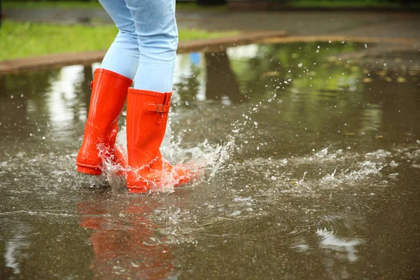 赤いゴムのブーツを持つ女性が水たまりに飛び込み、クローズアップ。雨天 — ストック写真