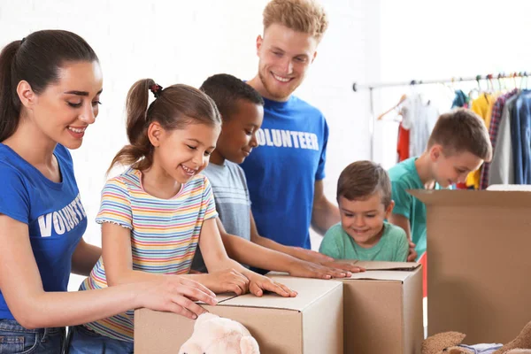 Voluntarios con niños clasificando bienes de donación en interiores — Foto de Stock